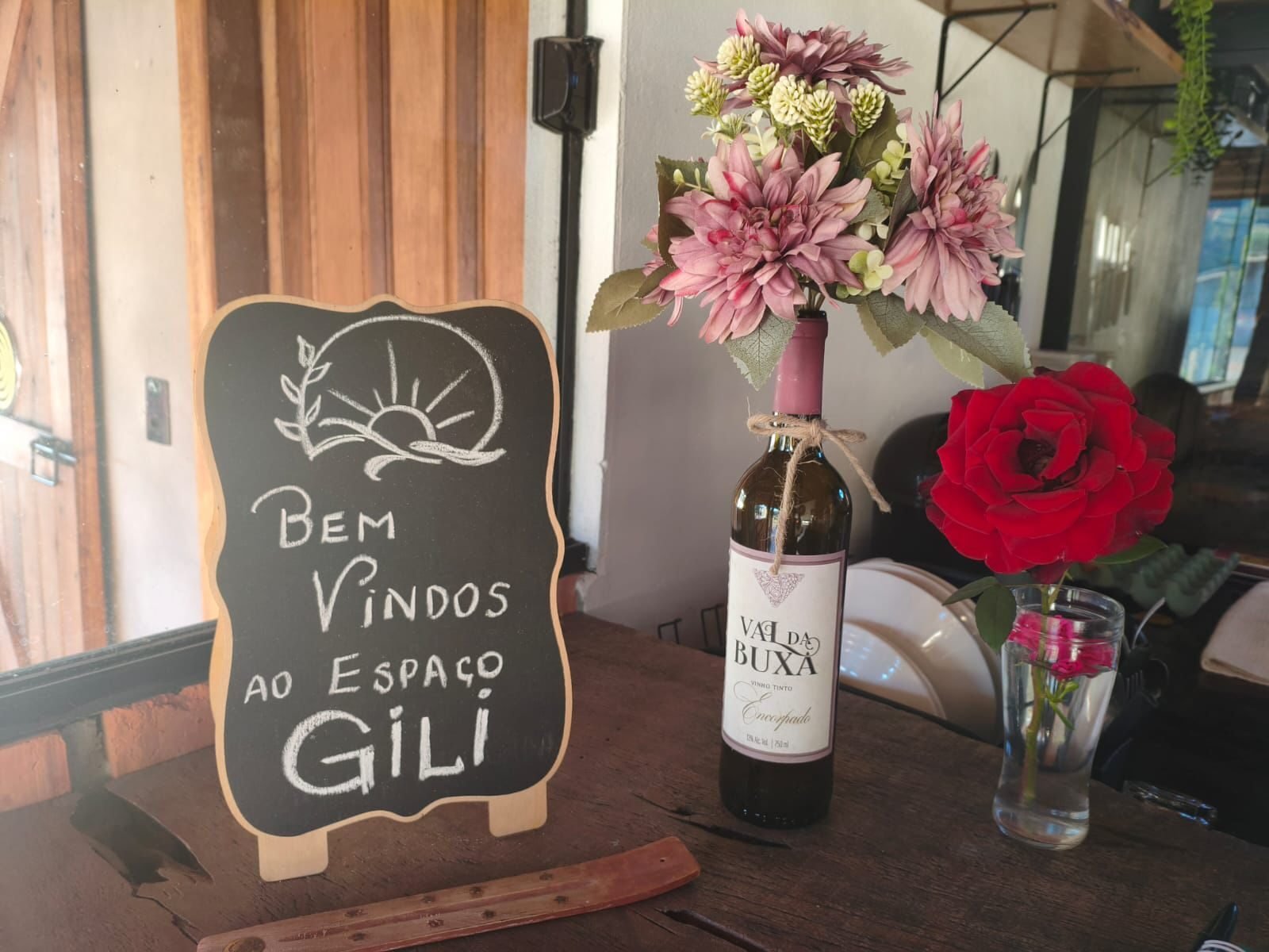 Placa de boas-vindas ao Espaço Gili com vinho e flores